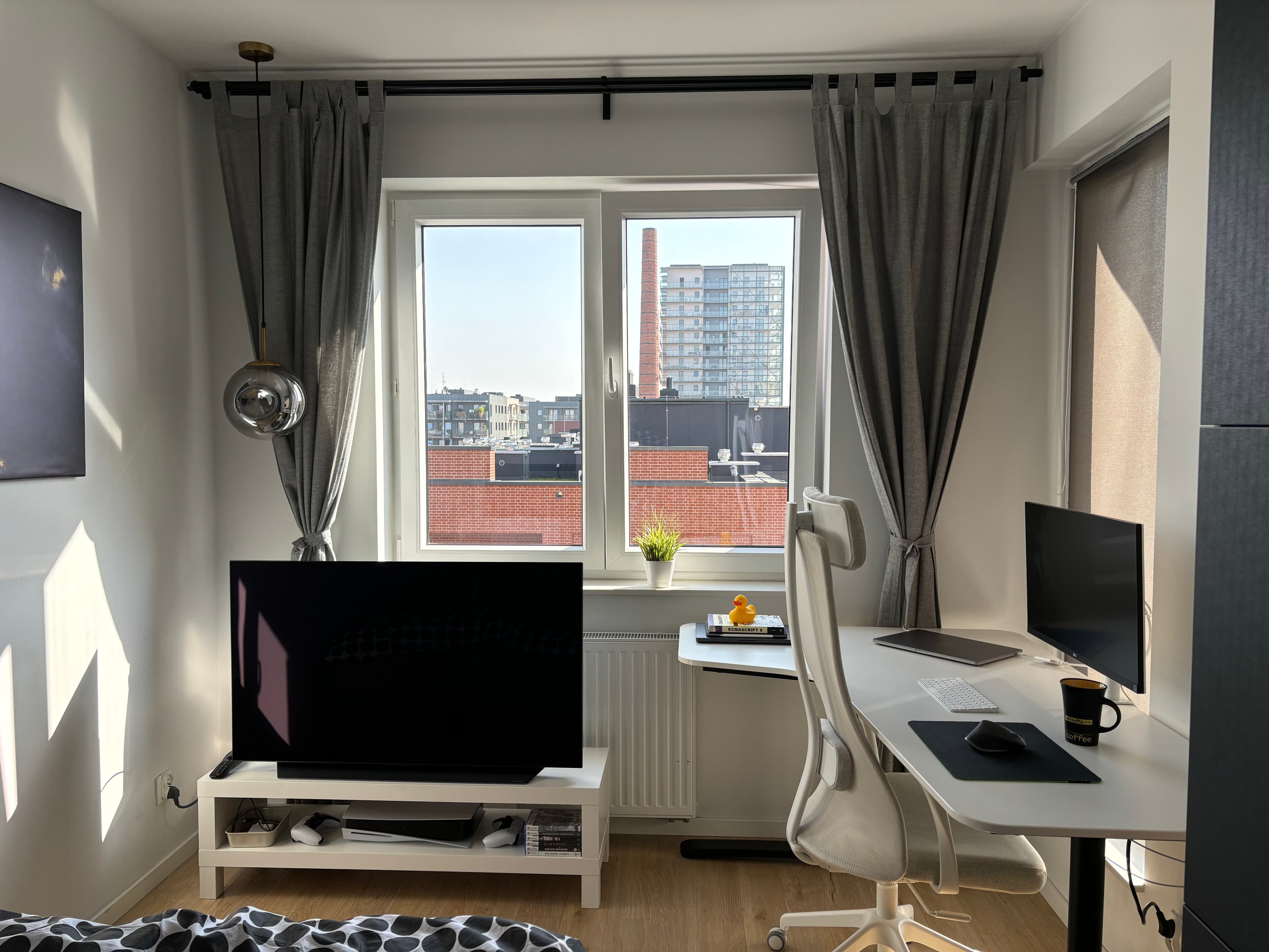 It is a panoramic view of my room. There is a wardrobe, a low TV cabinet, and a big corner desk. All furniture is black and white. The walls are white. The ceiling is also white with ball-shaped lamps hanging from it.