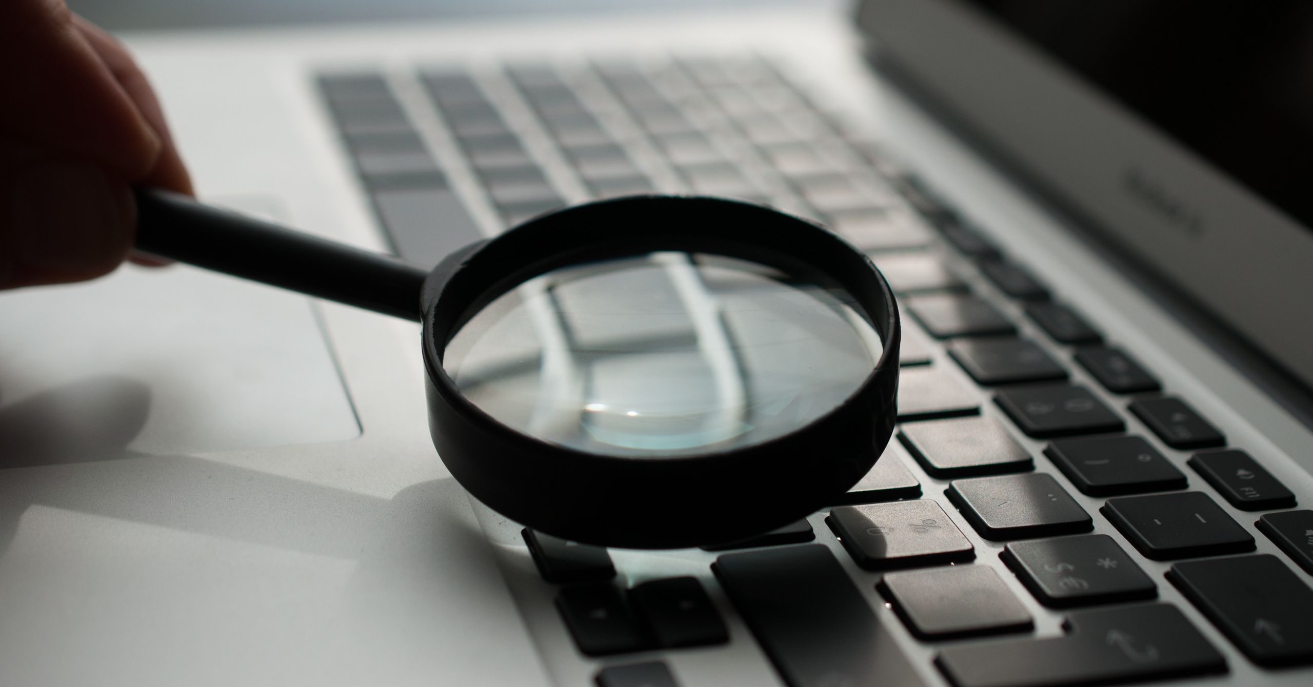 Hand with a magnifying glass inspecting the laptop keyboard