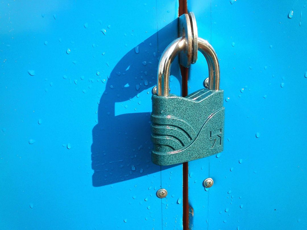 A sea-colored padlock closes a blue gate